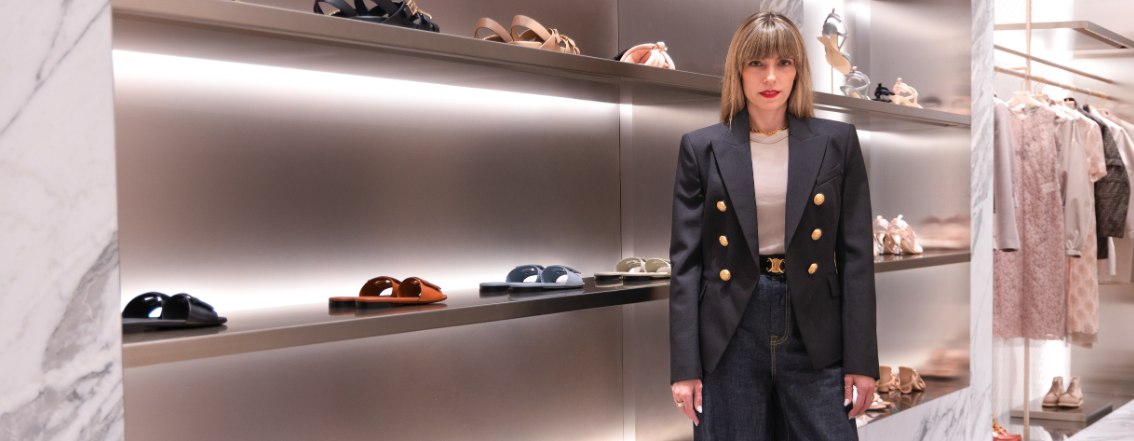 Raquel Macias, luxury personal stylist, standing confidently in a high-end boutique surrounded by designer footwear and elegant wardrobe displays.